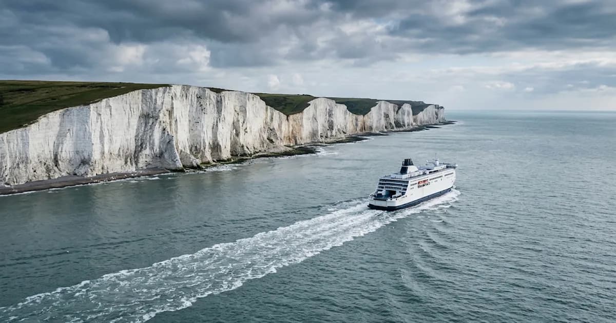 A ferry sailing away from white chalk cliffs across a grey sea